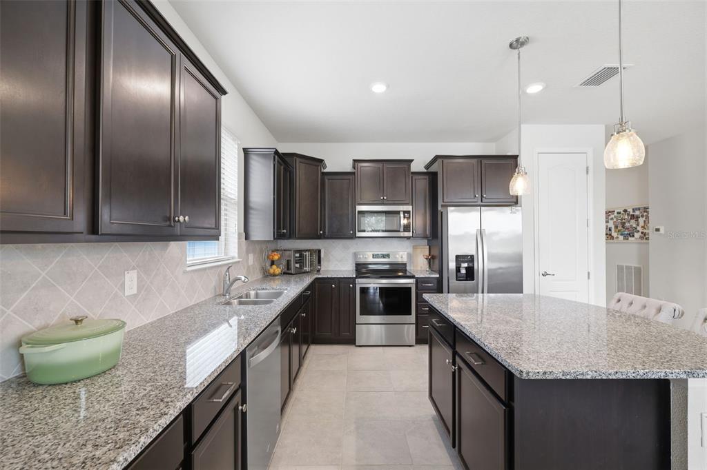 A kitchen with dark wood cabinets, granite countertops, stainless steel appliances, and a central island — 12929 PALAPA LOOP, SPRING HILL, FL