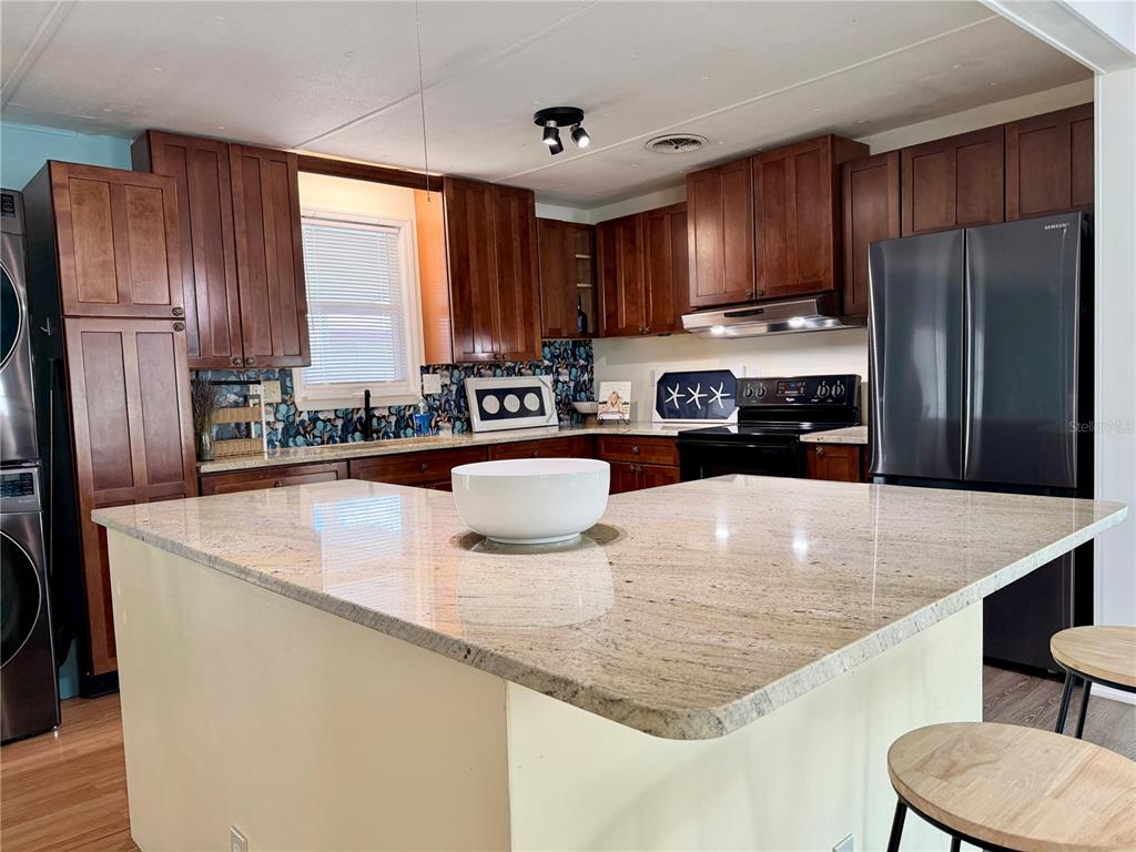An open-concept living area features light wood flooring, blue walls, and a kitchen island — 9790 66TH STREET N UNIT 100, PINELLAS PARK, FL