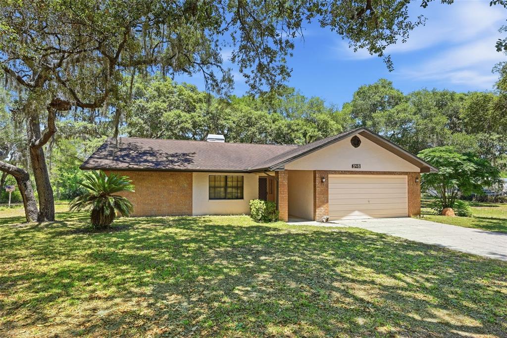 A single-story brick and stucco house with a two-car garage sits on a grassy lot — 3915 S SPANIEL TRAIL, INVERNESS, FL