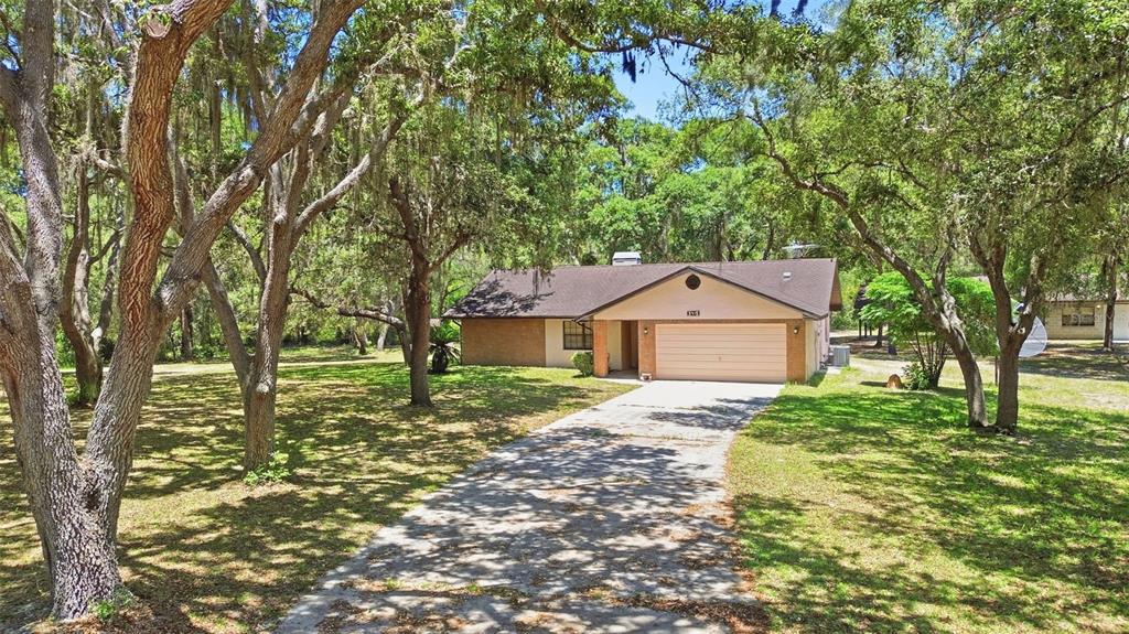 A single-story house with a beige exterior and a two-car garage sits among many trees — 3915 S SPANIEL TRAIL, INVERNESS, FL