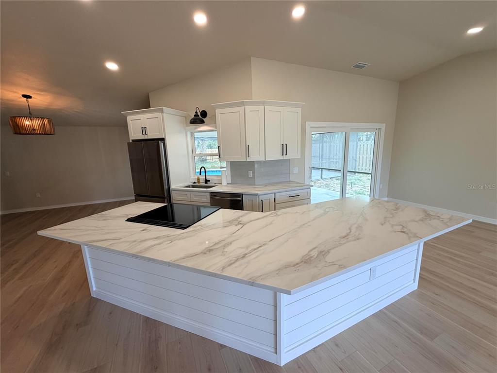 A kitchen features a large white marble-topped island, white cabinetry, and light wood flooring — 303 70TH STREET NW, BRADENTON, FL