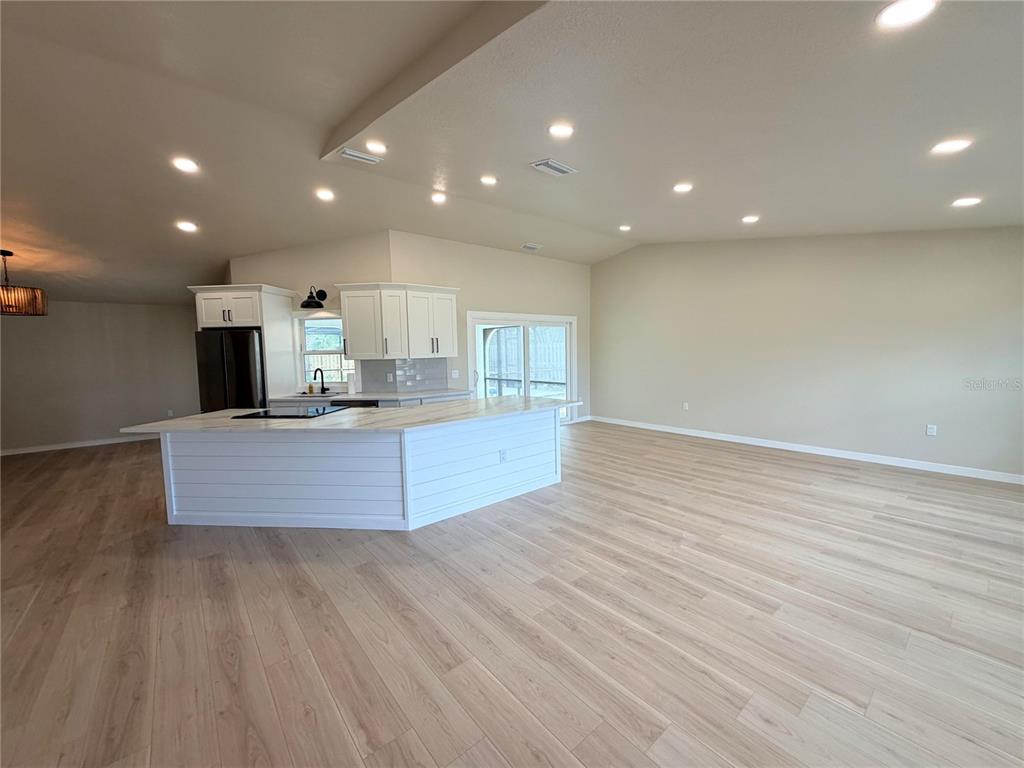 A kitchen with a white island and cabinetry opens into a spacious, light-floored living area — 303 70TH STREET NW, BRADENTON, FL