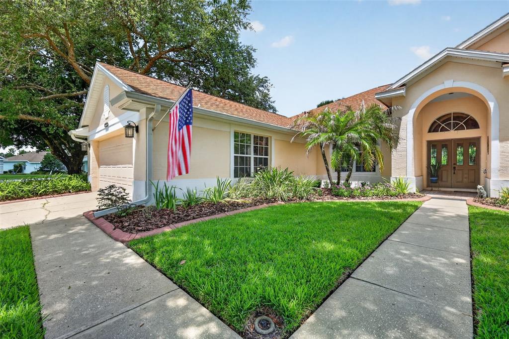 A single-story house with a beige stucco exterior, a front flag, and a paved walkway — 8059 LAUREL RIDGE DRIVE, MOUNT DORA, FL
