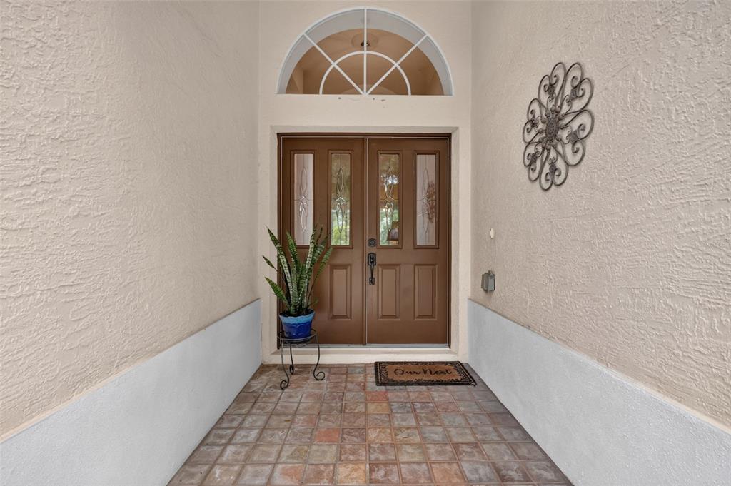A covered entryway features a double front door, a tiled floor, and a decorative wall hanging — 8059 LAUREL RIDGE DRIVE, MOUNT DORA, FL