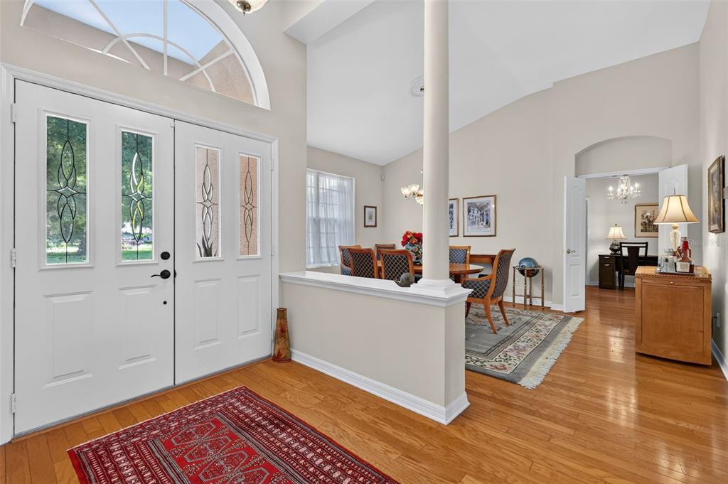 An entryway with a red rug, hardwood floors, and a partial wall opening to a dining room — 8059 LAUREL RIDGE DRIVE, MOUNT DORA, FL