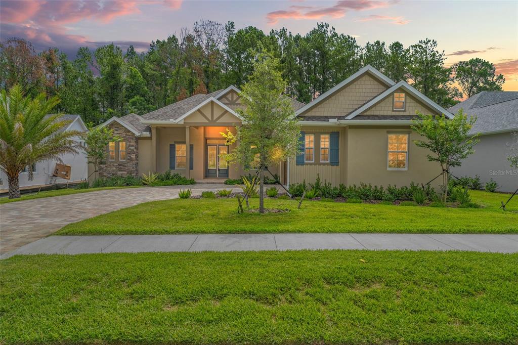 A single-story house with a stone facade, tan siding, and a paved driveway at dusk — 5034 ELM LEAF DRIVE, BROOKSVILLE, FL