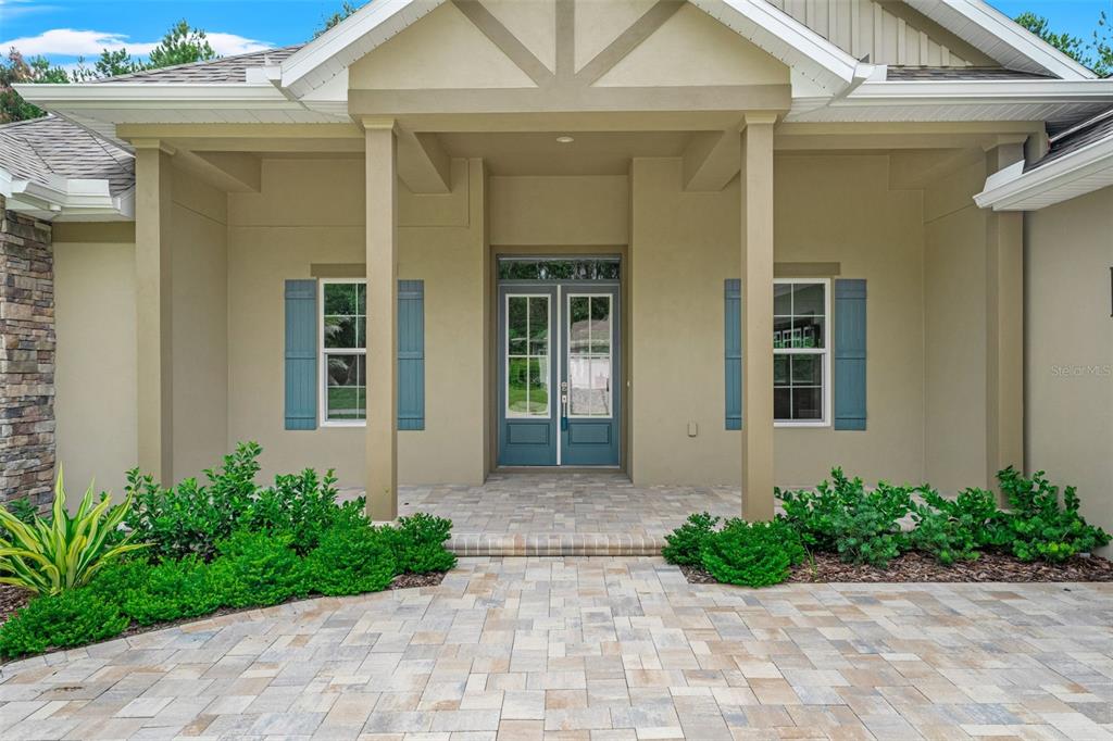 The exterior of a house features a paved walkway, double front doors, and blue shutters — 5034 ELM LEAF DRIVE, BROOKSVILLE, FL