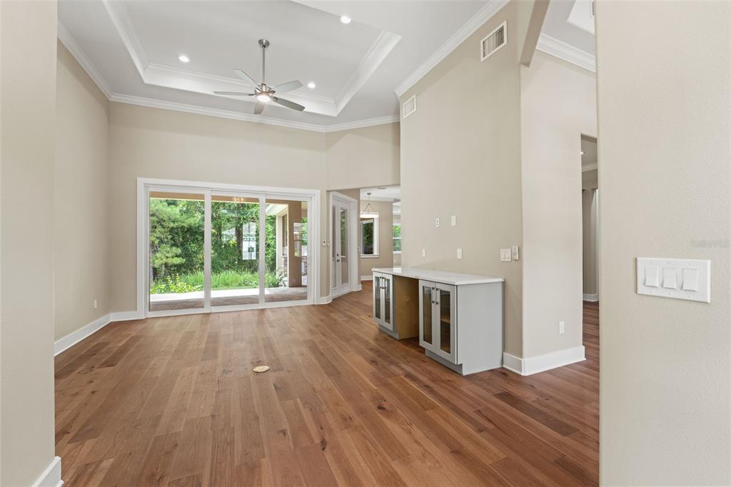A living room with hardwood floors, a tray ceiling, and sliding glass doors to a patio — 5034 ELM LEAF DRIVE, BROOKSVILLE, FL