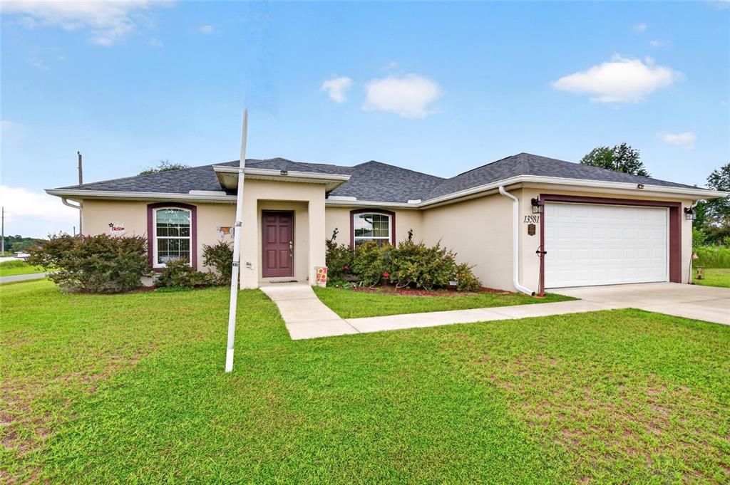 A single-story house with a white garage, a brown front door, and an American flag — 13581 SW 48TH COURT, OCALA, FL