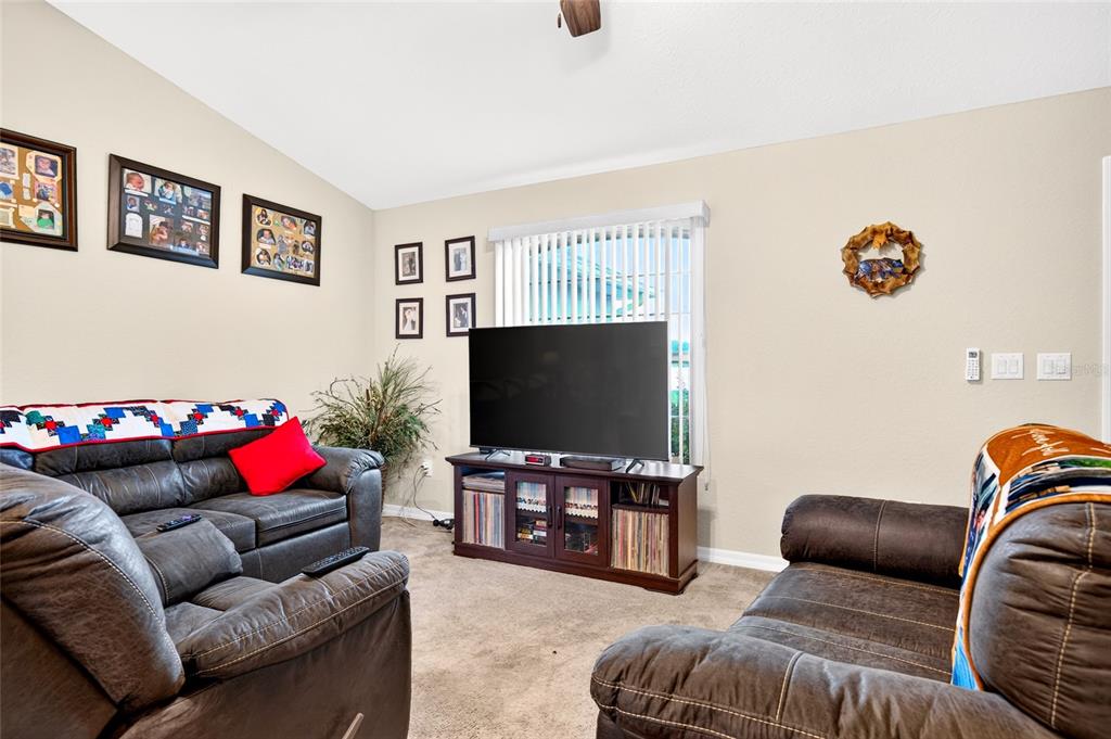 A living room features gray carpeting, dark leather furniture, and a vaulted ceiling with a fan — 13581 SW 48TH COURT, OCALA, FL