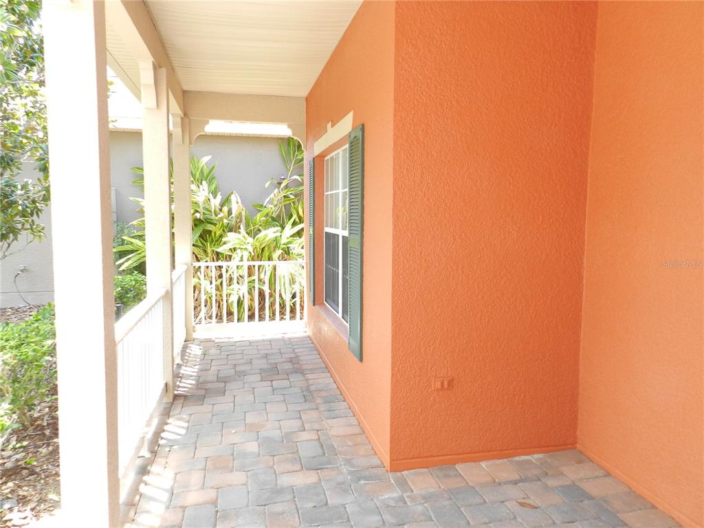 A covered porch features orange stucco walls, a paver floor, and a white railing — 542 PORTOFINO DRIVE, POINCIANA, FL