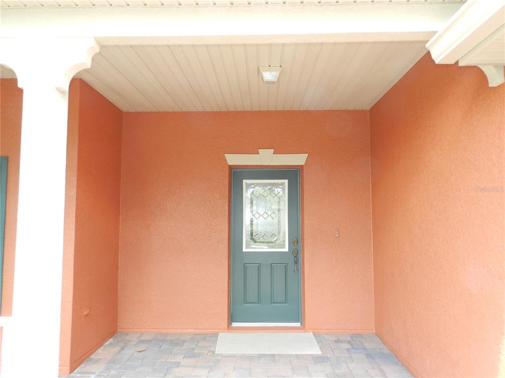 A covered front porch with a teal door and a paved floor — 542 PORTOFINO DRIVE, POINCIANA, FL