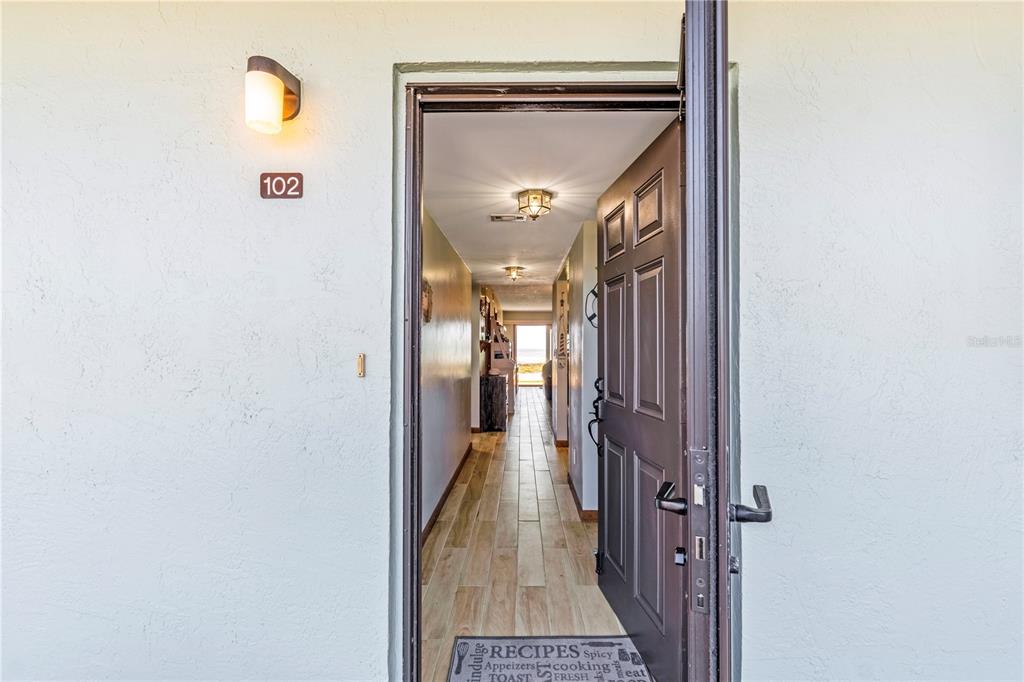 An open front door reveals a hallway with wood-look flooring leading to a sunlit room — 2222 OCEAN SHORE BOULEVARD UNIT 102B, ORMOND BEACH, FL