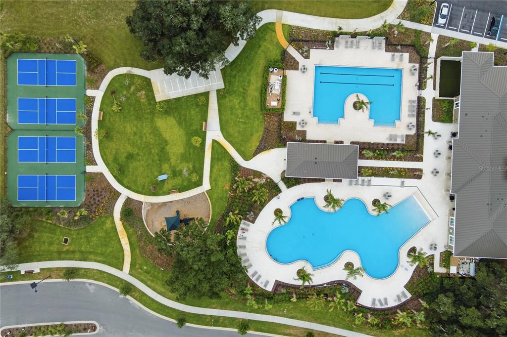 An aerial view shows a community amenity center with two swimming pools and four pickleball courts — 8371 GOWER TRAIL, WILDWOOD, FL
