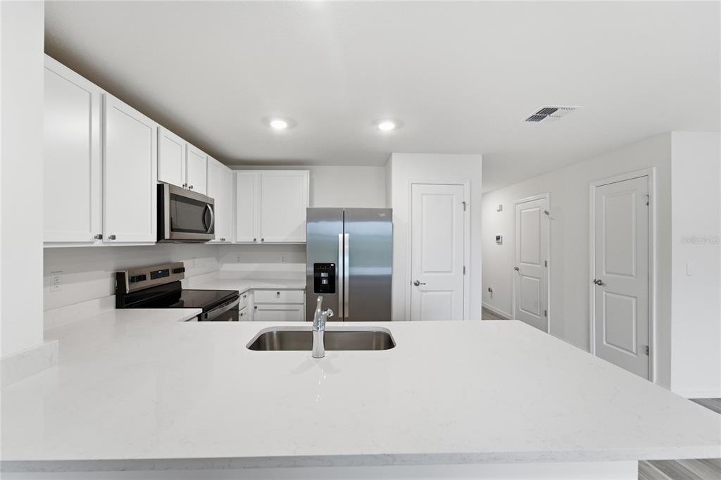 A kitchen features white cabinets, stainless steel appliances, and a large white quartz countertop island — 8371 GOWER TRAIL, WILDWOOD, FL