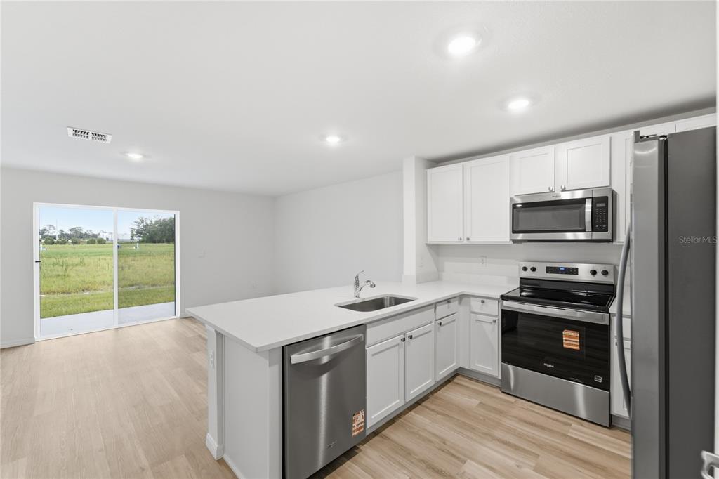 A modern kitchen with white cabinets, stainless steel appliances, and a sliding glass door — 8371 GOWER TRAIL, WILDWOOD, FL