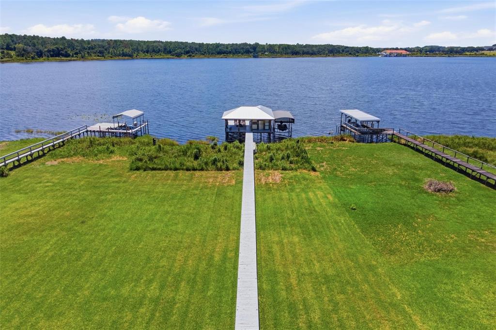 An aerial view of a long wooden dock extending into a lake from a grassy lawn — 3716 BAYSHORE CIRCLE, TAVARES, FL