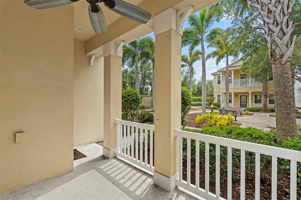 A covered porch with a ceiling fan overlooks a landscaped courtyard and a neighboring building — 514 WINTERSIDE DRIVE, APOLLO BEACH, FL