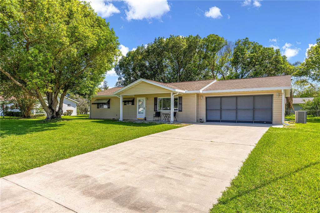 A single-story house with tan siding, a concrete driveway, and a large tree in front — 10765 SW 62ND TERRACE, OCALA, FL