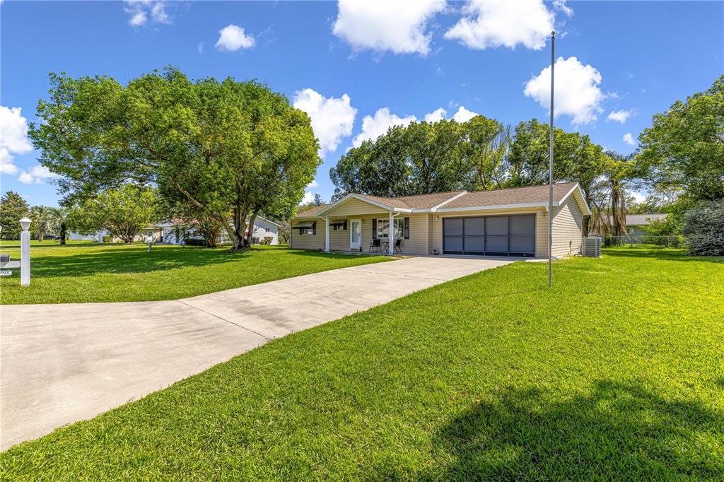 A single-story house with beige siding, a concrete driveway, and a large front lawn — 10765 SW 62ND TERRACE, OCALA, FL