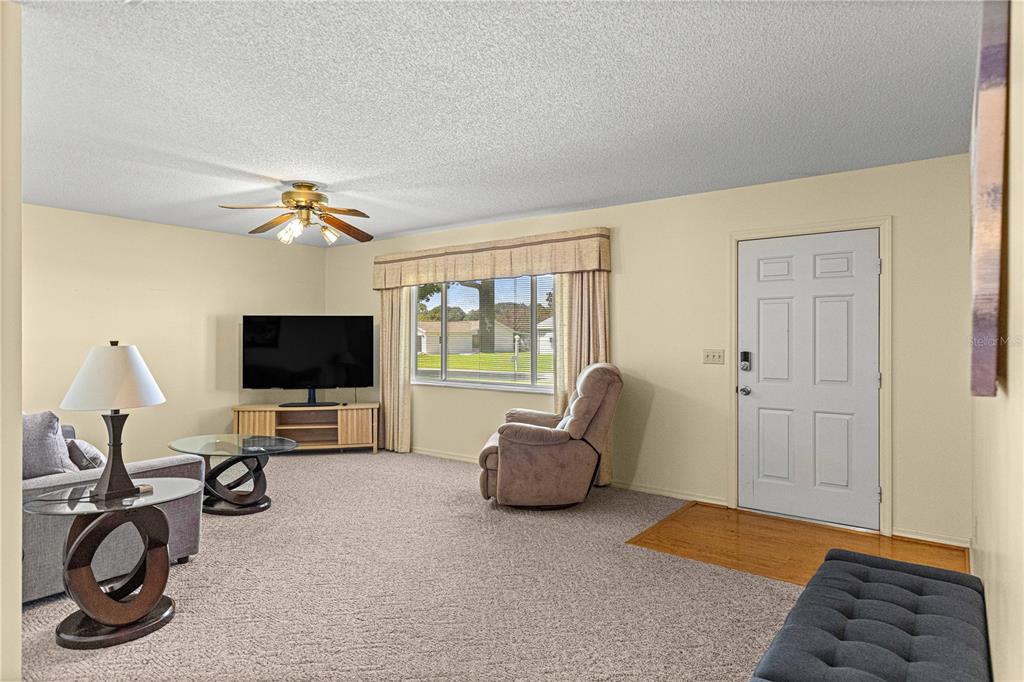 A living room features carpeted flooring, a ceiling fan, a television, and an entryway door — 10765 SW 62ND TERRACE, OCALA, FL