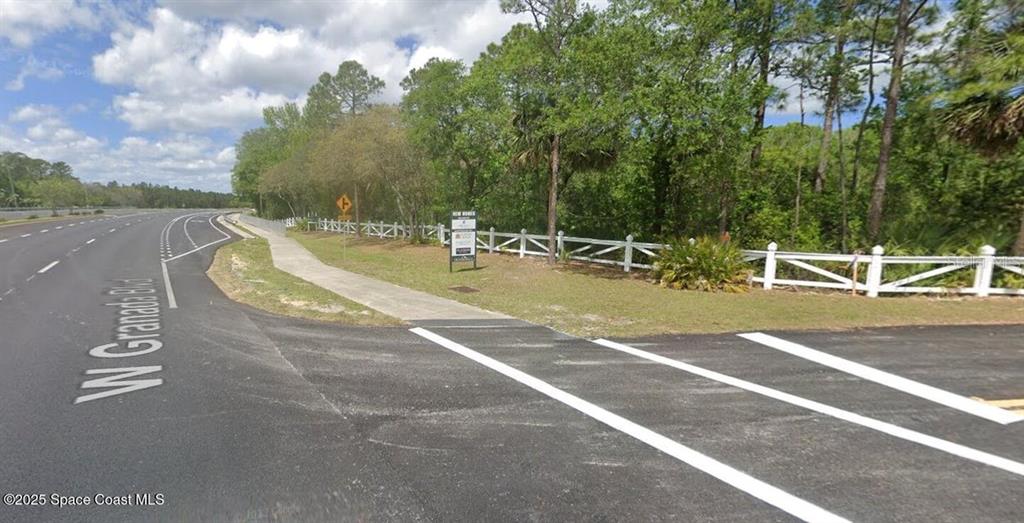 A paved road and sidewalk run alongside a white fence bordering a wooded area — W SR-40, ORMOND BEACH, FL