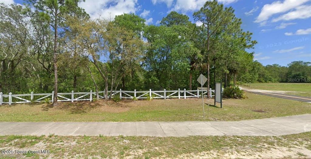 A white fence borders a wooded lot next to a sidewalk and a paved road — W SR-40, ORMOND BEACH, FL