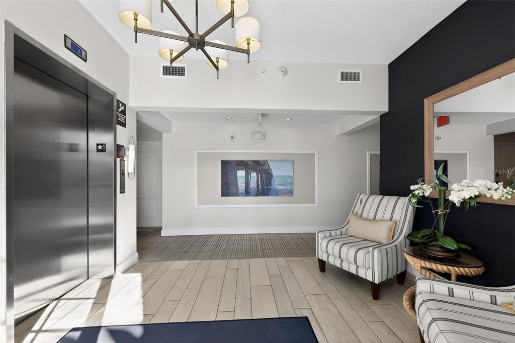 A modern elevator lobby features light tile flooring, a chandelier, and striped armchairs — 915 BAY COLONY DRIVE S UNIT S, JUNO BEACH, FL