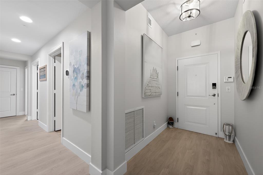 A bright entryway features light wood-look flooring, white walls, a front door, and wall art — 915 BAY COLONY DRIVE S UNIT S, JUNO BEACH, FL