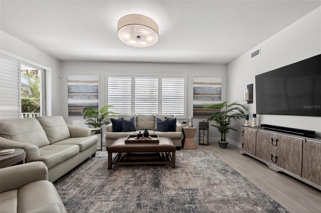 A living room features light-colored sofas, a large area rug, and a wall-mounted television — 915 BAY COLONY DRIVE S UNIT S, JUNO BEACH, FL