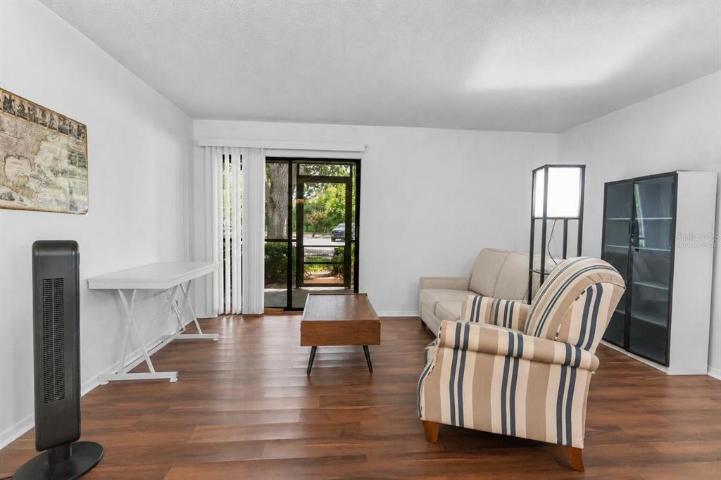 A living room features wood-look flooring, a sliding glass door, and a striped armchair — 6018 LAKTREE LANE UNIT E, TEMPLE TERRACE, FL
