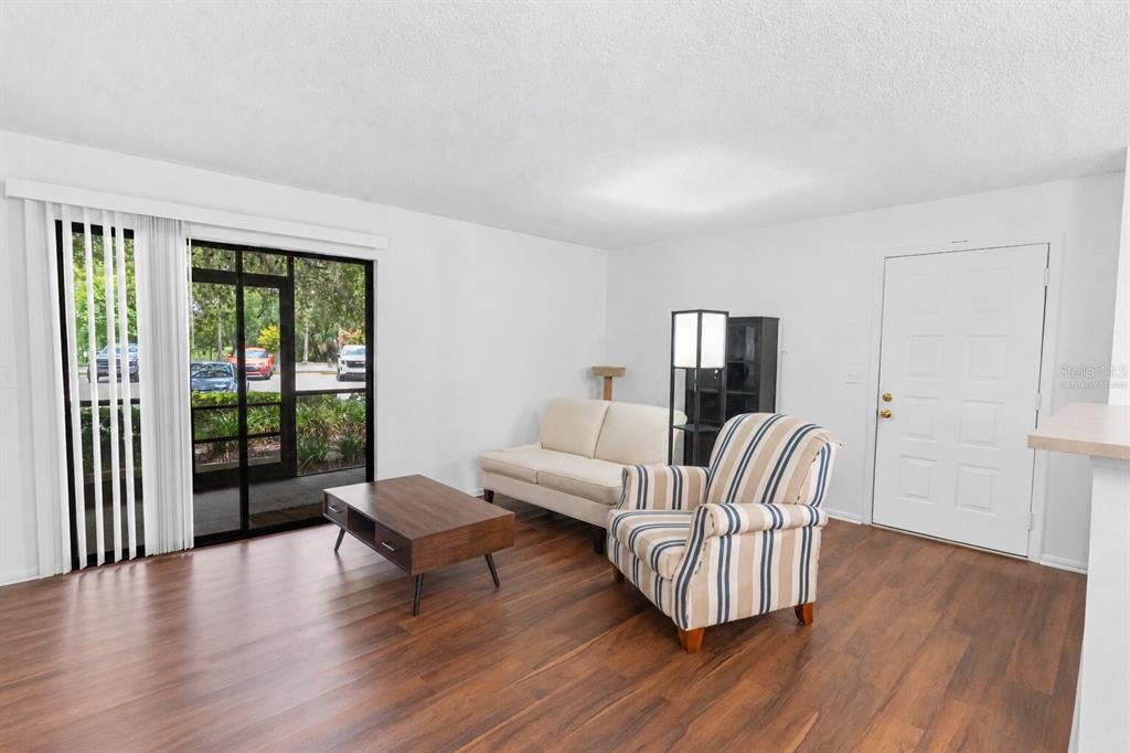 A living room features wood-look flooring, a sliding glass door, a sofa, and an armchair — 6018 LAKTREE LANE UNIT E, TEMPLE TERRACE, FL