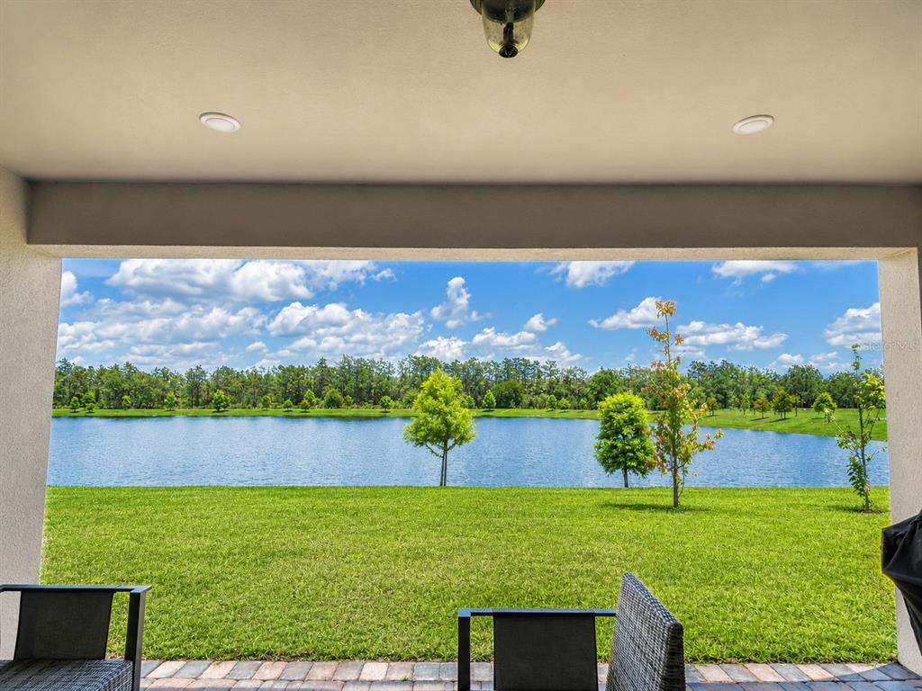 A covered patio overlooks a grassy lawn and a lake under a blue sky — 4891 SHADY PINES DRIVE, ST CLOUD, FL