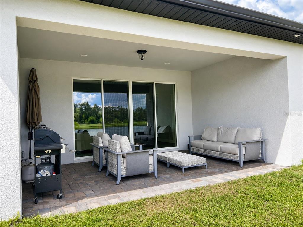 A covered patio features a paved floor, outdoor furniture, and a grill overlooking a pond — 4891 SHADY PINES DRIVE, ST CLOUD, FL