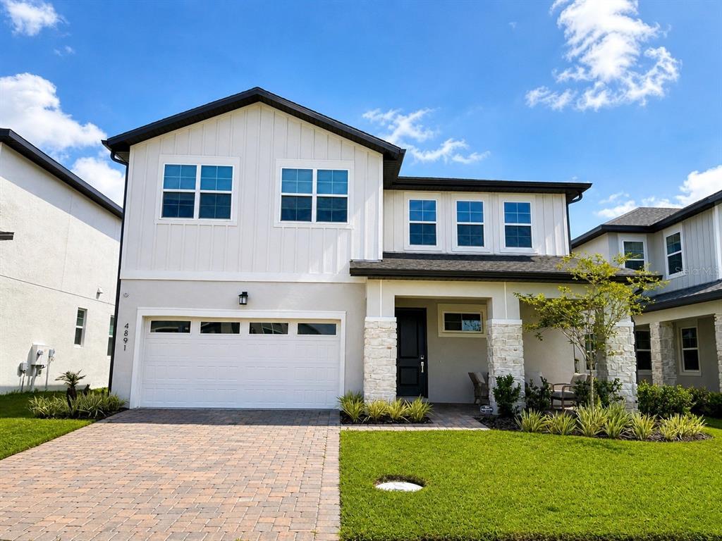 A two-story house with a white board-and-batten facade, stone accents, and a paved driveway — 4891 SHADY PINES DRIVE, ST CLOUD, FL