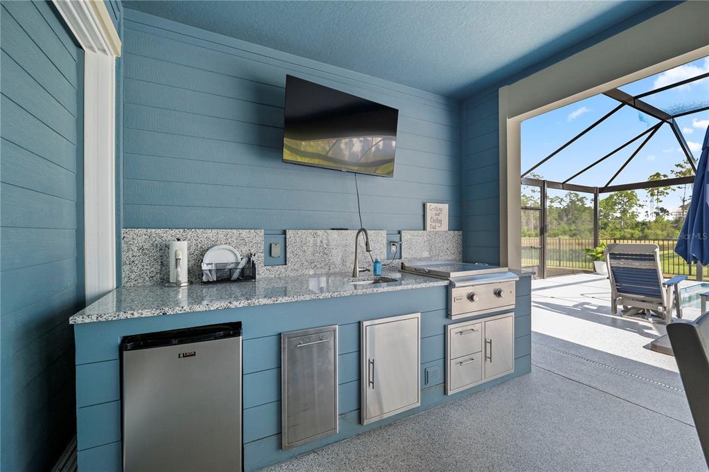 An outdoor kitchen features blue paneled walls, granite countertops, a stainless steel grill, and a refrigerator — 2453 GLADE LANE, GREEN COVE SPRINGS, FL