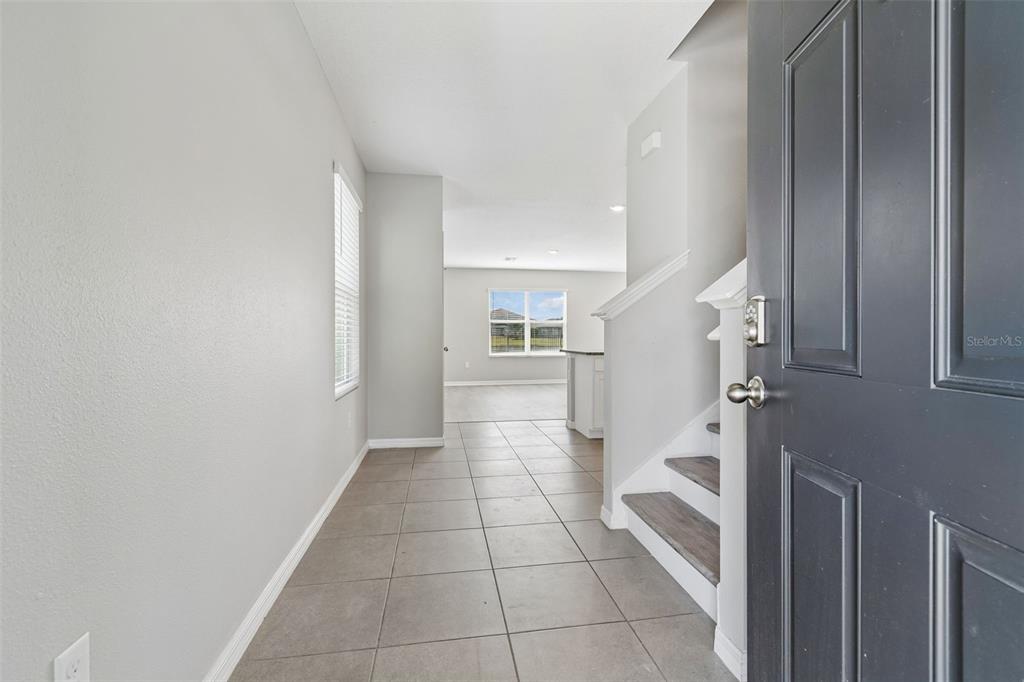 An entryway features gray tile flooring, a staircase with wood treads, and a view beyond — 16734 TRITE BEND STREET, WIMAUMA, FL