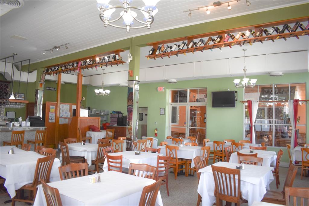A restaurant dining room features white-clothed tables, wooden chairs, and wine bottles displayed on wall racks — 1618 E 5TH AVENUE, TAMPA, FL
