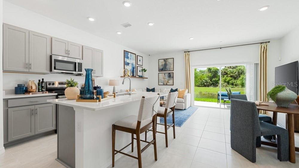 A modern kitchen with gray cabinets and a white island opens to a living area — 7125 PINELIT COVE, NOKOMIS, FL