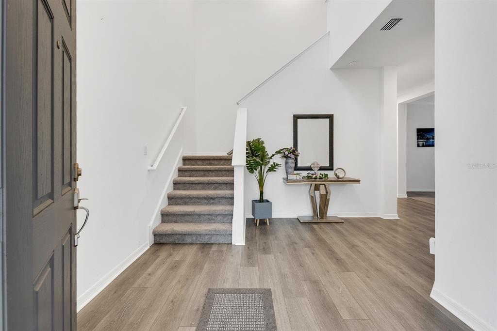 An entryway features light wood-look flooring, a carpeted staircase, and a modern console table — 31867 ASBURY AVENUE, WESLEY CHAPEL, FL