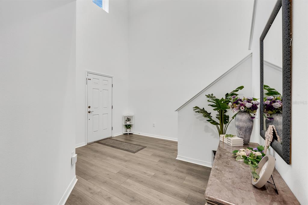 A bright entryway features high ceilings, wood-look flooring, a white door, and a staircase — 31867 ASBURY AVENUE, WESLEY CHAPEL, FL