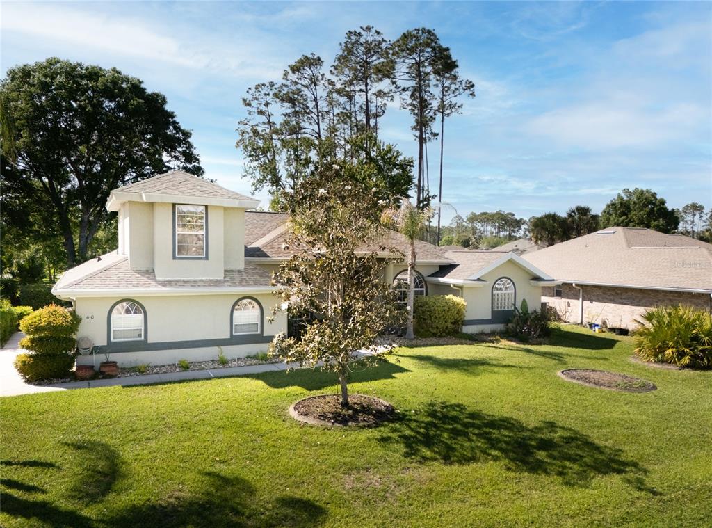 An exterior view of a light-colored house with a lawn and tall pine trees — 40 EDGEWATER DRIVE, PALM COAST, FL