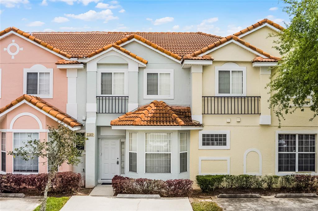 A multi-story townhouse exterior with a tiled roof, light-colored stucco walls, and a small balcony — 1149 S BEACH CIRCLE, KISSIMMEE, FL