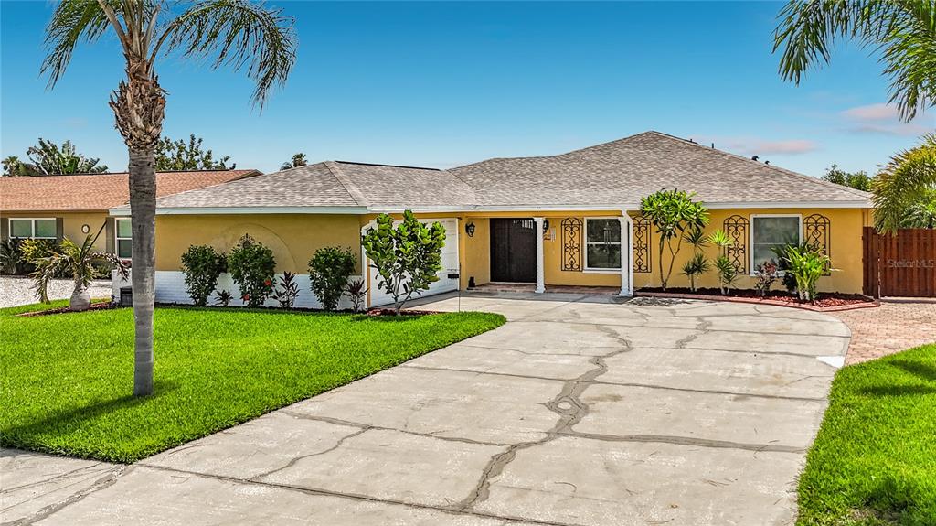 A single-story yellow house with a cracked concrete driveway and palm trees in the yard — 6517 SOLITAIRE PALM WAY, APOLLO BEACH, FL