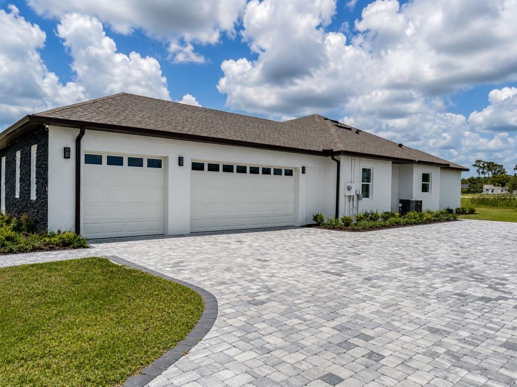 A white house with a three-car garage and a large paver driveway under a cloudy sky — 29121 CAN DO LANE, TAVARES, FL