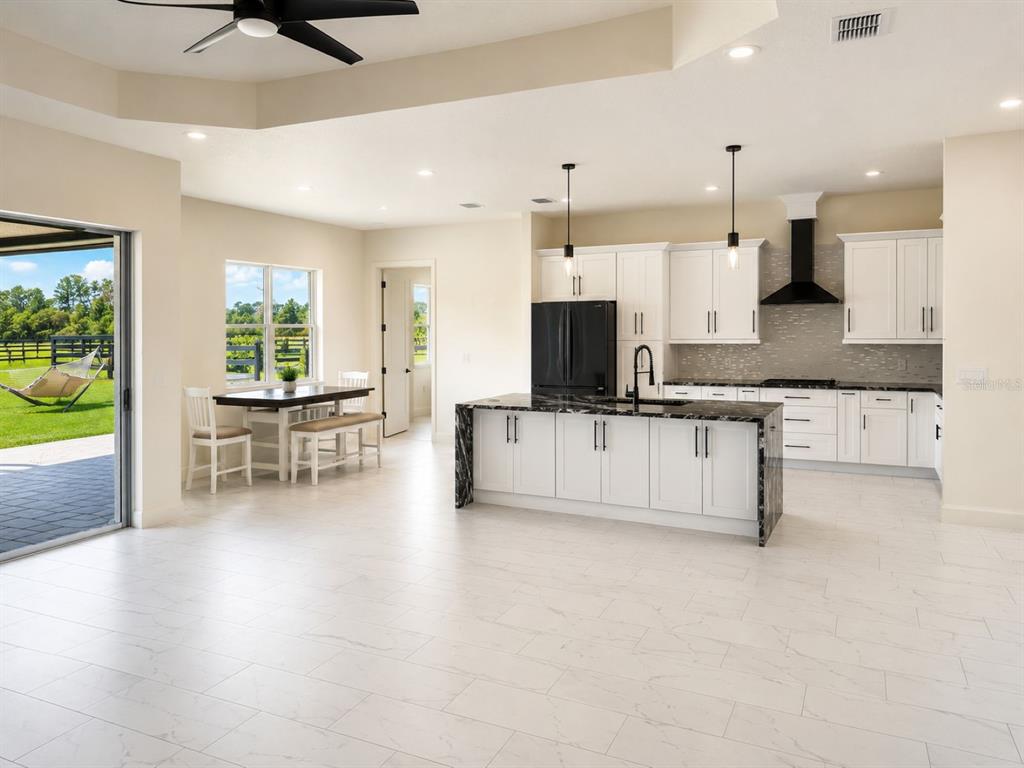 A modern kitchen with white cabinets, a dark marble island, and an adjacent dining area — 29121 CAN DO LANE, TAVARES, FL