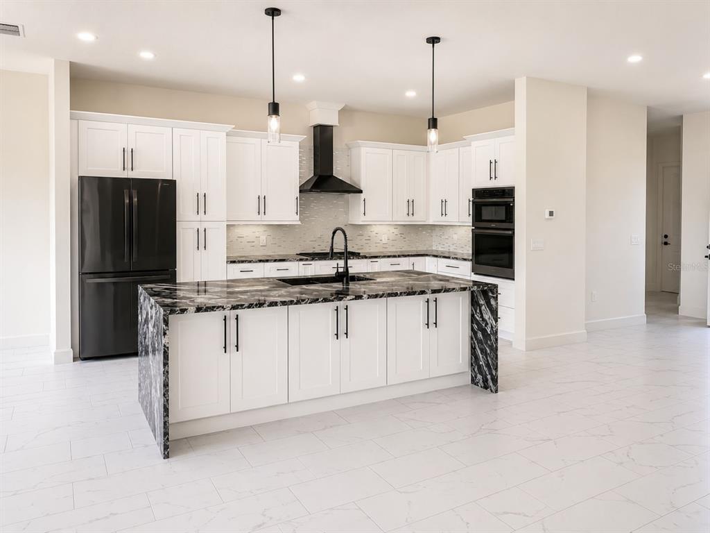 A modern kitchen features white cabinets, a black waterfall island, and black stainless steel appliances — 29121 CAN DO LANE, TAVARES, FL