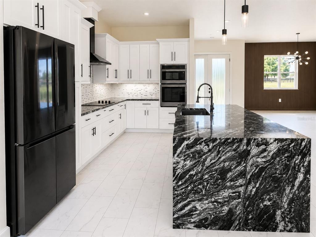 A modern kitchen features white cabinetry, black appliances, and a large black-and-white marble island — 29121 CAN DO LANE, TAVARES, FL