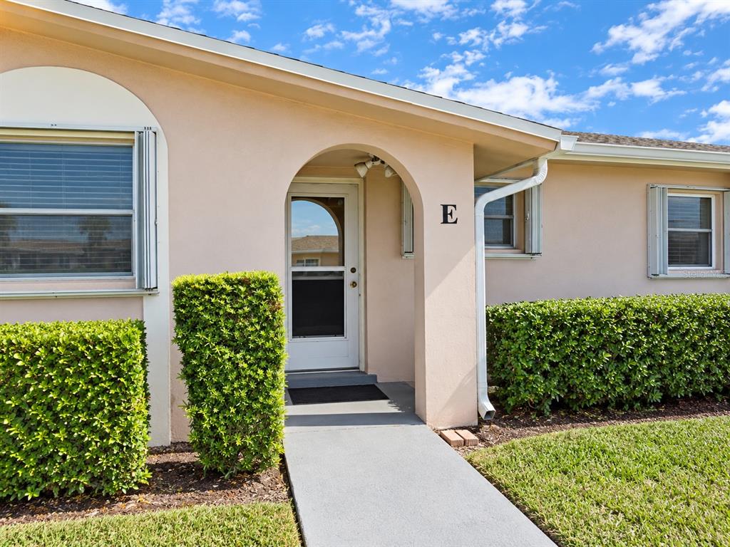The exterior of a light-colored building features an arched entryway labeled with the letter E — 2784 DUDLEY DRIVE E UNIT E, WEST PALM BEACH, FL