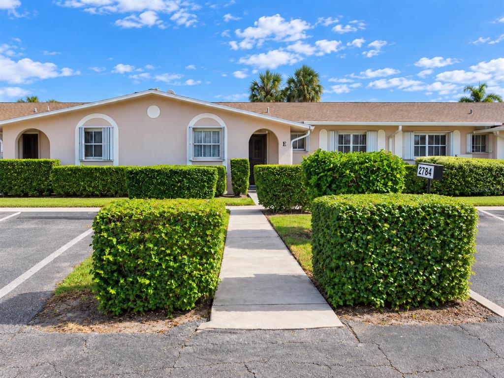 A single-story residential building with light-colored stucco walls and manicured hedges along the walkway — 2784 DUDLEY DRIVE E UNIT E, WEST PALM BEACH, FL